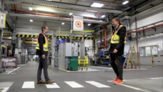 Zwei Mitarbeiter begegnen sich im Lager, während sie die Linde Secure Distance Vest und den Linde Distance Beeper tragen.
