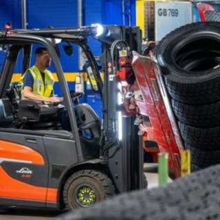 Mitarbeiter von Michelin Tyre PLC greift einen Reifenstapel mit einer am Gabelstapler montierten Klammer.