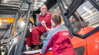 Unsere Mitarbeiter spielen eine zentrale Rolle in unserer Nachhaltigkeitspolitik. Eine Servicetechnikerin reicht einer anderen Servicetechnikerin im Gabelstapler ein Werkzeug.
