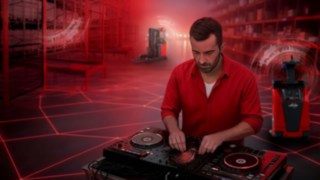 Ein DJ steht in einer Lagerhalle am Mischpult, im Hintergrund befinden sich automatisierte Fahrzeuge von Linde Material Handling.
