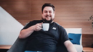 Ein Mitarbeiter mit Kaffeetasse in der Hand wirkt entspannt und freundlich, während er aktiv in der Inbetriebnahme bei Linde tätig ist. 
