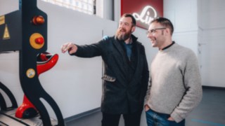 Automatisierungsexperten tauschen sich vor einem Linde-Fahrzeug aus, was für kollaborative Teamarbeit, globalen Wissensaustausch und kundenzentrierte Automatisierungslösungen steht. 
