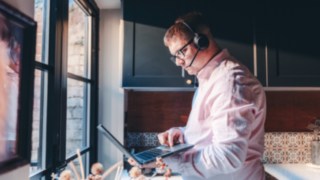 Ein Mitarbeiter mit Headset arbeitet im Homeoffice am Laptop und demonstriert die flexible Arbeitsweise im Bereich Intralogistik und Automation. 