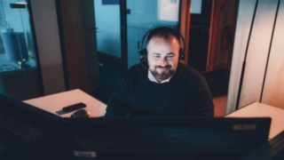 Projektmanager mit Headset arbeitet am Bildschirm und gibt einen Einblick in den Arbeitsalltag bei Linde im Bereich Intralogistik und Automation. 