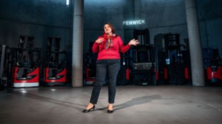Eine Mitarbeiterin hält eine Präsentation in einem modernen Industrieumfeld mit Linde-Gabelstaplern im Hintergrund, was für internationale Zusammenarbeit, interkulturellen Austausch und globale Karrieremöglichkeiten in einem weltweit vernetzten Unternehmen steht. 